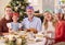 Portrait Of Multi-Generation Family Celebrating Christmas At Home Wearing Paper Hats Before Meal 