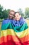 portrait of multiethnic couple of women carrying lgbti pride flag and smiling at the camera outdoors