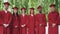 Portrait of multiethnic group of graduating students standing outdoors wearing red gowns and mortar-boards, smiling and