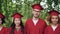 Portrait of multinational group of graduating students in red graduation gowns and mortar-boards standing together