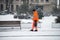 Portrait of municipal employee throwing road salt on the sidewalk in the street by snowy day