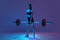 Portrait of muscled woman in sportswear training with a barbell isolated on purple background in neon light. Sport