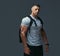 Portrait of a muscular handsome bodybuilder in sportswear with rucksack posing against a gray background.