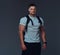 Portrait of a muscular handsome bodybuilder in sportswear with rucksack posing against a gray background.