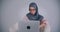 Portrait of muslim businesswoman in hijab and glasses typing on laptop attentively raises eyes to camera and smiles.