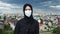 Portrait Muslim woman in black hijab wearing protective medical face mask posing over Islamic city