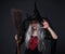 Portrait of mysterious woman in black witch halloween costume and hat with broom posing over black