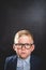 Portrait of nerd smart school child with thumb up near blackboard blank and looking at camera. Happy kid boy in uniform