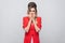 Portrait of nervous beautiful business lady with hairstyle and makeup in red fancy blazer, standing biting her nails and looking