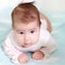 Portrait of newborn Caucasian baby holding head, leaning on arms, brown eyes, blond hairs