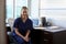 Portrait Of Nurse Wearing Scrubs Sitting At Desk In Office