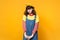 Portrait of offended disconcerted girl teenager in french beret, denim sundress standing isolated on yellow wall