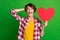 Portrait offunny lady arm behind head heart figure open mouth style checkered shirt isolated on green color background