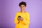 Portrait ofpleased african american man smiling and holding smartphone, wearing bluetooth earphones, isolated over violet