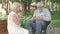 Portrait of old positive paralyzed man sharing apples with smiling beautiful woman sitting on bench in sunny summer park