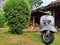 portrait of an old vespa motorbike in the yard with a view of the joglo house