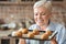 Portrait of old woman presenting tray with self made croissants