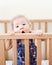 Portrait of one cute adorable funny baby of nine months standing in bed crib chewing eating sucking wooden sides