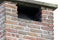 A portrait of the opening or smoke exit top part of a tall masonry grout red brick chimney on a roof of a house on an overcast day