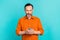 Portrait of optimistic focused man dressed orange shirt read post in social media on smartphone isolated on turquoise