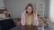 Portrait of overburdened overwhelmed young woman rubbing temples holding head in hands sitting at table indoors