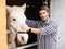 Portrait of an owner of livestock farm next to horse in a stall in the backyard of farm