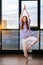 Portrait of peaceful redhead young woman does yoga asana raising hands in namaste mudra while standing near large window