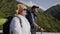 Portrait of a pensioners with backpacks and hiking sticks cheerfully walking on a road with mountains in the backdrop