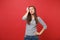 Portrait of pensive bewildered young woman in striped clothes looking up, keeping hand on head isolated on bright red