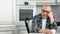 Portrait of pensive gray-haired casual elderly man sitting at white kitchen during coffee break