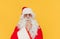 Portrait of a pensive Santa Claus in glasses standing and wearing a hat standing on a yellow background and looking at the camera