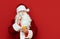 Portrait of pensive santa claus on red background holding smartphone and looking into camera. Funny Santa uses smartphone isolated