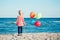 Portrait of pensive teenager white Caucasian child kid with colorful bunch of balloons, standing on beach on sunset