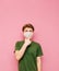 Portrait of a pensive young man in a green t-shirt and white medical mask isolated on a pink background, looking up at copy space