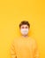 Portrait of a pensive young man in a yellow sweater and white medical mask isolated on a yellow background, looking up at copy