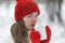 Portrait of pensive young woman in red hat and mittens in snowy park. Beautiful young woman drink hot beverage from cup in winter
