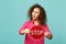 Portrait of perplexed african girl in pink casual clothes holding text board STOP isolated on blue turquoise wall