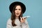 Portrait photo of Beautiful young asking dissatisfied brunette woman wearing black hat and grey sweater holding