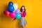 Portrait photo of surprised amazed girl holding colorful air balloons keeping hand neat face with opened mouth smiling