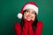Portrait photo of young toothy beaming smile chinese girl wear santa hat touch cheeks dreamy look empty space isolated