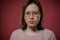 Portrait of a plain woman in glasses against a red wall.