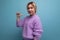 portrait of pleasant charming pleasant blond young woman in purple sweater pointing finger at herself on blue background