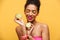 Portrait of pleased afro american woman with trendy makeup holding two halves of fresh lime in both hands isolated, over yellow b