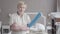 Portrait of positive adult Caucasian woman in uniform posing in clean hotel room. Confident blond maid crossing hands