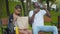 Portrait of positive African American brother and sister having snack in summer park. Cheerful girl giving water and bun