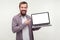 Portrait of positive bearded man in casual plaid shirt holding laptop and pointing at empty screen. white background, place for ad
