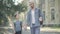 Portrait of positive Caucasian brothers walking along schoolyard in sunlight. Smiling young man and cute little boy