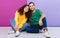 Portrait of positive caucasian couple in colorful clothing smiling and hugging together while sitting on floor