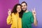 Portrait of positive caucasian couple man and woman in colorful clothing smiling while showing peace fingers