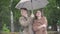 Portrait of positive Caucasian handsome man smiling and hugging loving girlfriend on rainy day outdoors. Middle shot of